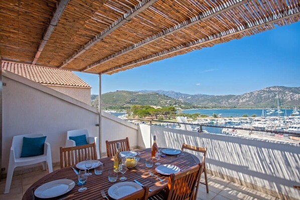 A terrace with a table set for dining, overlooking a marina and hills.