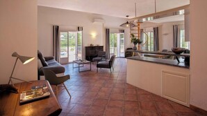 A spacious living area with a sofa, armchair, and coffee table. A kitchen area with a dining table and bar counter is visible. Large windows provide natural light and views of the outdoors. - Casa Catarelli. (Farinole)