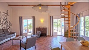 A spacious living room with a wooden spiral staircase, a large window with a view, a sofa, a coffee table, and a dining table. - Casa Catarelli. (Farinole)