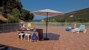 An outdoor patio with a table and chairs, a large umbrella, and lounge chairs. - Casa Catarelli. (Farinole)