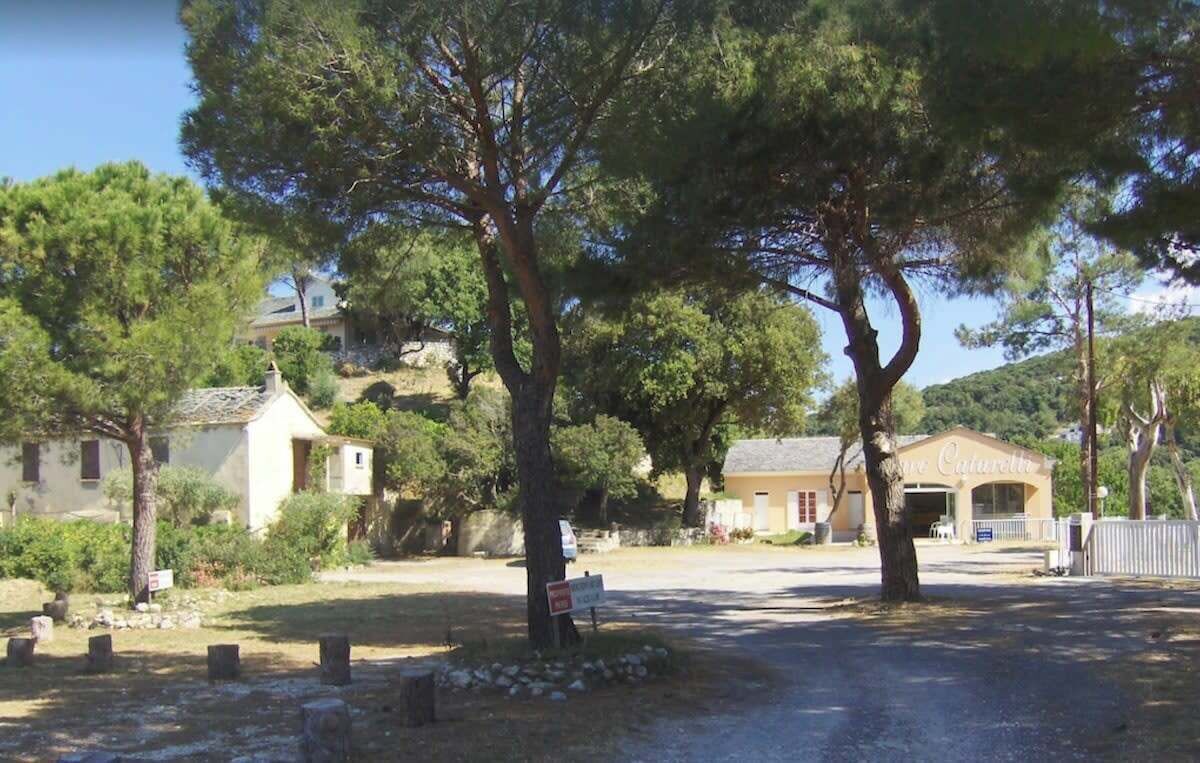Un entorno rural con un pequeño edificio que parece una casa de huéspedes o una posada, rodeado de árboles y un sendero de tierra.