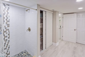Un baño con paredes de azulejos blancos, ducha con puerta de vidrio y suelo de baldosas.