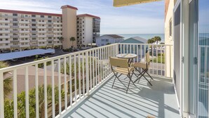 A balcony with a table and chairs, overlooking a parking area and a building with multiple balconies.