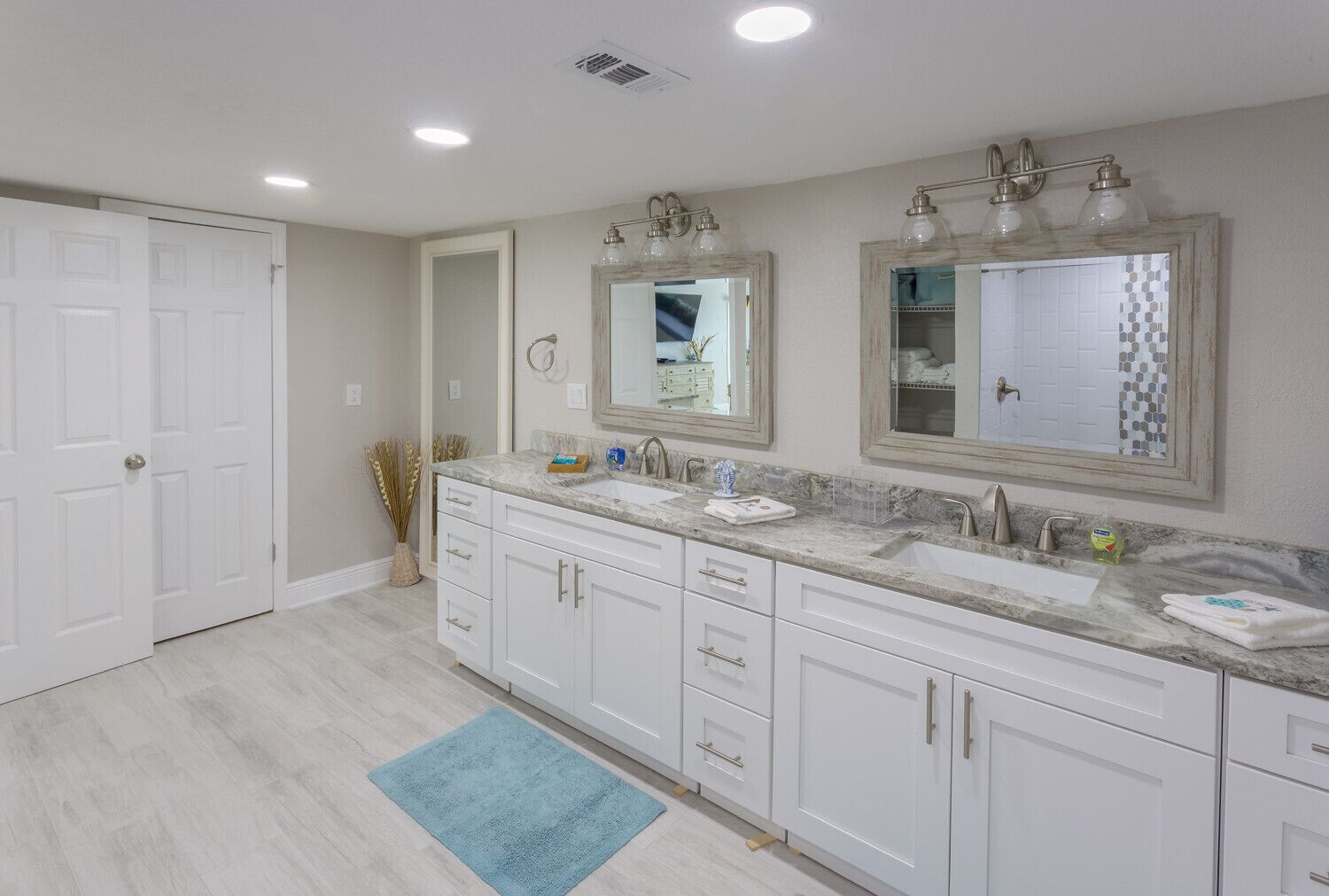Un baño moderno con muebles blancos, encimera de mármol, dos lavamanos y un espejo grande con marco decorativo.