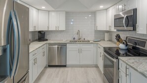 A modern kitchen with white cabinets, stainless steel appliances, and a marble countertop.