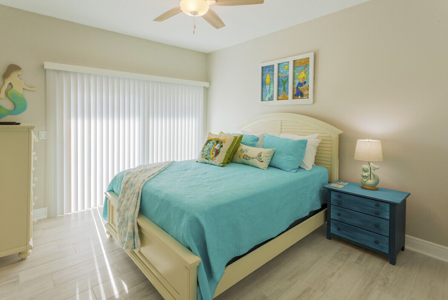 A bedroom with a bed, a nightstand, a lamp, a window with blinds, and a ceiling fan.