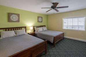 A hotel room with two beds, a ceiling fan, a window with blinds, and patterned carpet.