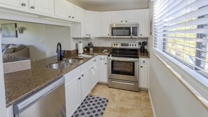 Una cocina moderna con armarios blancos, electrodomésticos de acero inoxidable y una ventana con persianas.