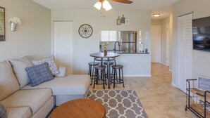 A living room with a sofa, coffee table, and a ceiling fan. There is a kitchen area with a refrigerator and a dining table with stools. - La Casa Del Mar 608 Star5vacationscom (Dunedin)