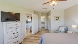 A bedroom with a bed, a dresser, a ceiling fan, a nightstand, and a view into the kitchen. - La Casa Del Mar 608 Star5vacationscom (Dunedin)