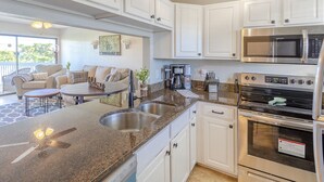A modern kitchen with white cabinets, a granite countertop, stainless steel appliances, and a dining area with a sofa and coffee table. - La Casa Del Mar 608 Star5vacationscom (Dunedin)