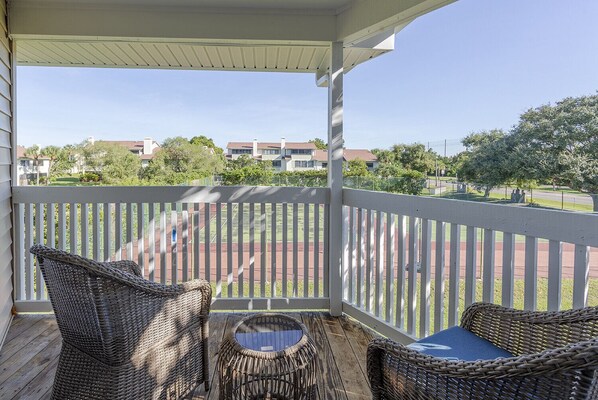 A covered balcony with wicker furniture and a view of a playground and buildings in the background.