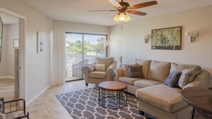 A living room with a ceiling fan, a sofa, a coffee table, and a chair. There is a sliding glass door leading to a balcony. - La Casa Del Mar 602 Star5vacations (Dunedin)
