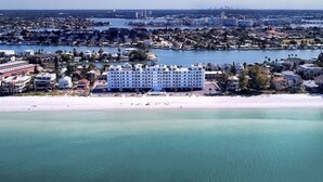 Un hotel frente al mar con varios pisos, una playa en primer plano y un puerto deportivo al fondo.