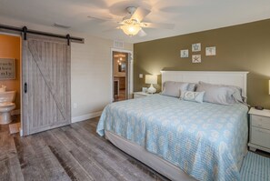 Un dormitorio con cama, mesita de noche, ventilador de techo y una puerta corredera de estilo rústico.