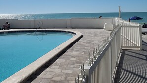 Piscina con vistas al océano, rodeada por una valla blanca y un deck de baldosas.
