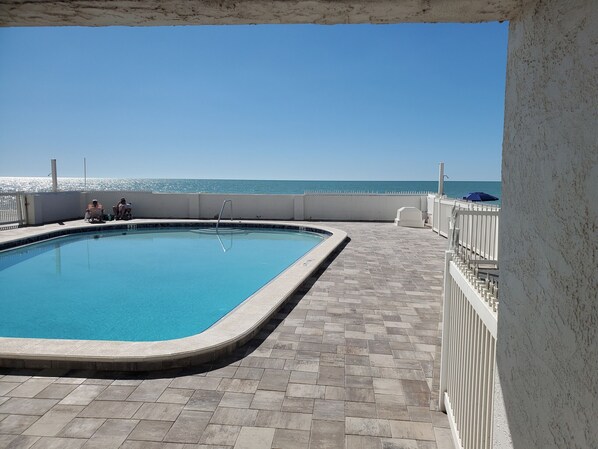 Una piscina rectangular con solárium empedrado, una escalera metálica y vista al océano.