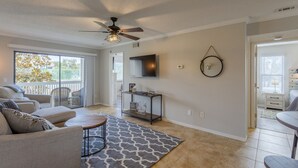 A spacious living room with a ceiling fan, a large TV, and a sliding glass door leading to a balcony. - La Casa Del Mar 604 Star5vacations (Dunedin)