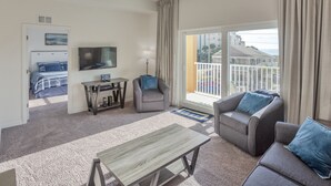 A modern living room with a sofa, armchair, and coffee table. A television is mounted on the wall, and a door leads to a bedroom. - Madeira Bay 1302 Star5vacations (Madeira Beach)