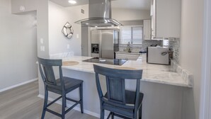 Cozinha moderna com ilha central, dois banquetes, eletrodomésticos de aço inoxidável e coifa de vidro.