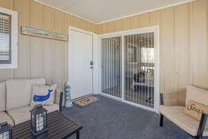 Un espacio interior acogedor con un sofá color beige, una mesita con un farol, y un ventanal corredizo que da a un área exterior.