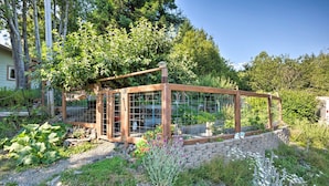 A wooden structure with a glass enclosure, surrounded by a garden with various plants and a stone wall. - Quaint Riverside Reprieve w/ Kayaks + Floats! (Brookings)
