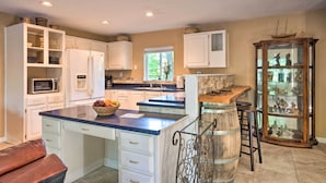 A kitchen with white cabinets, a central island with a sink, a microwave, and a fruit bowl. - Quaint Riverside Reprieve w/ Kayaks + Floats! (Brookings)
