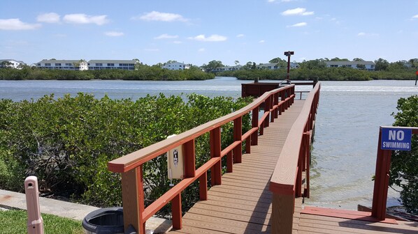 A wooden pier with a 'NO SWIMMING' sign, leading to a body of water with buildings in the background. - Beautiful Seashell/ Pool Star5vacations (Indian Shores)