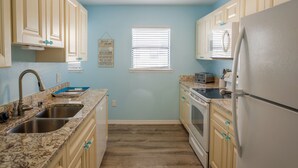 A kitchen with light blue walls, wooden cabinets, a stainless steel sink, and a white refrigerator. - Beautiful Seashell/ Pool Star5vacations (Indian Shores)
