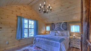 A cozy wooden cabin bedroom with a large bed, a chandelier, and a decorative rug. - Treehouse Ellijay Star5vacations (Ellijay)