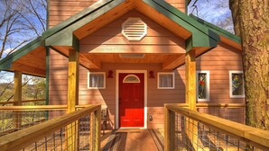 A wooden cabin with a red door, a covered porch, and a small window with a view of the surrounding landscape. - Treehouse Ellijay Star5vacations (Ellijay)