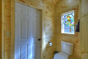 A wooden-paneled bathroom with a white toilet, a wooden door, and a stained glass window depicting a bird.