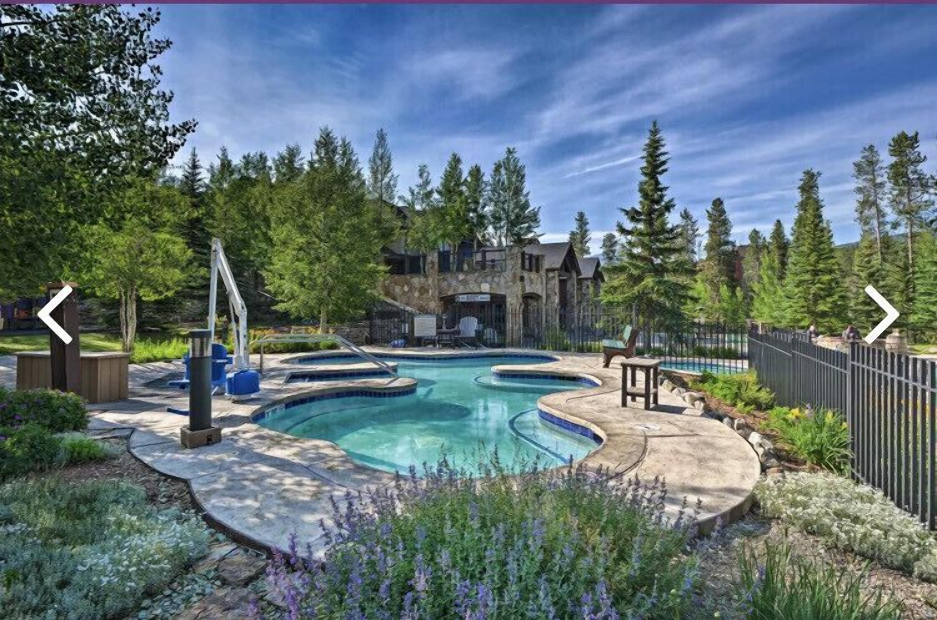 A swimming pool with a stone deck, surrounded by trees and a wooden deck area.
