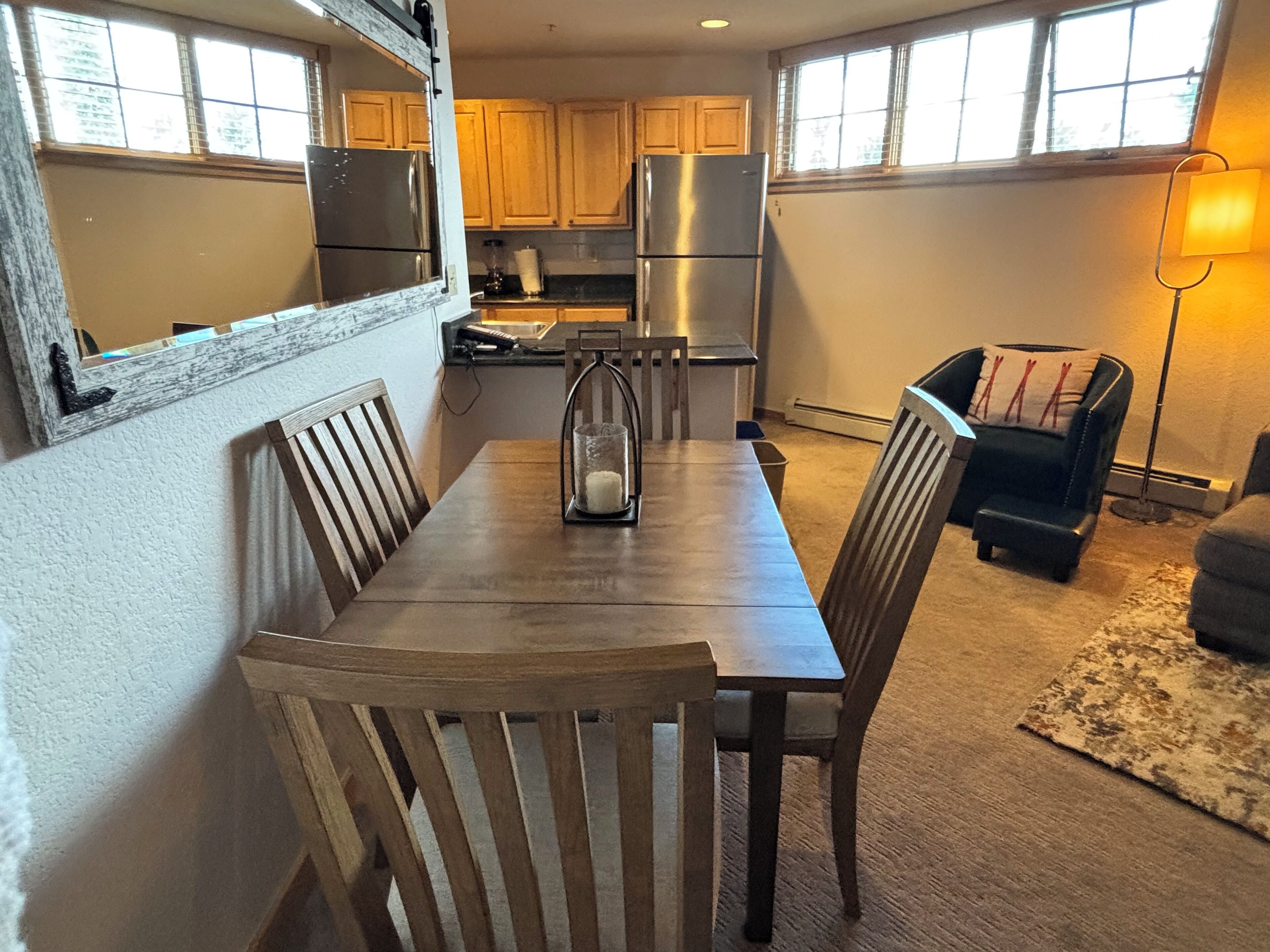 A compact kitchen with wooden cabinets, a stainless steel refrigerator, and a dining area with a wooden table and chairs.