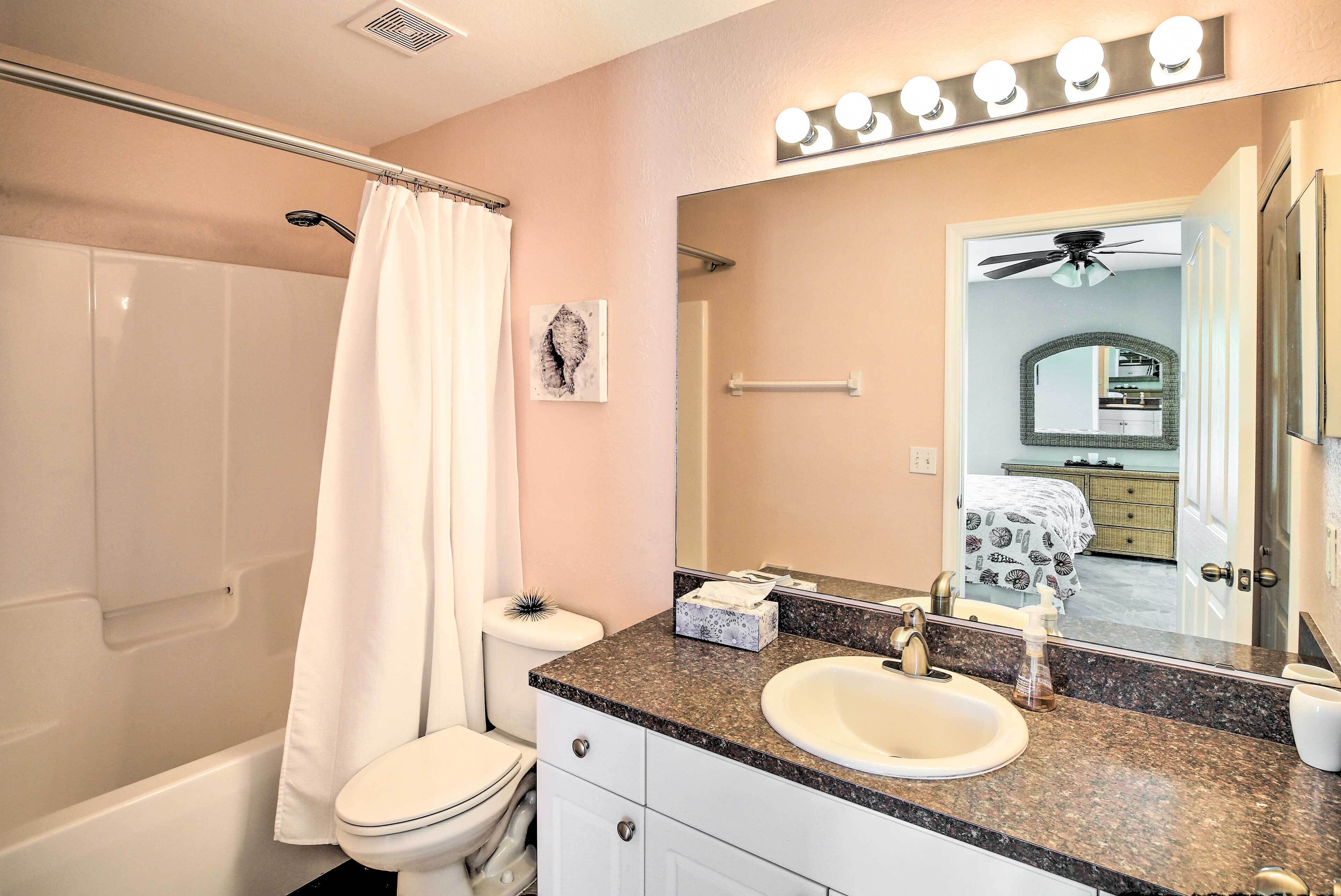 A bathroom with a bathtub, toilet, sink, and a large mirror with lights above.