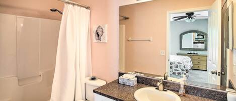 A bathroom with a bathtub, toilet, sink, and a large mirror with lights above.