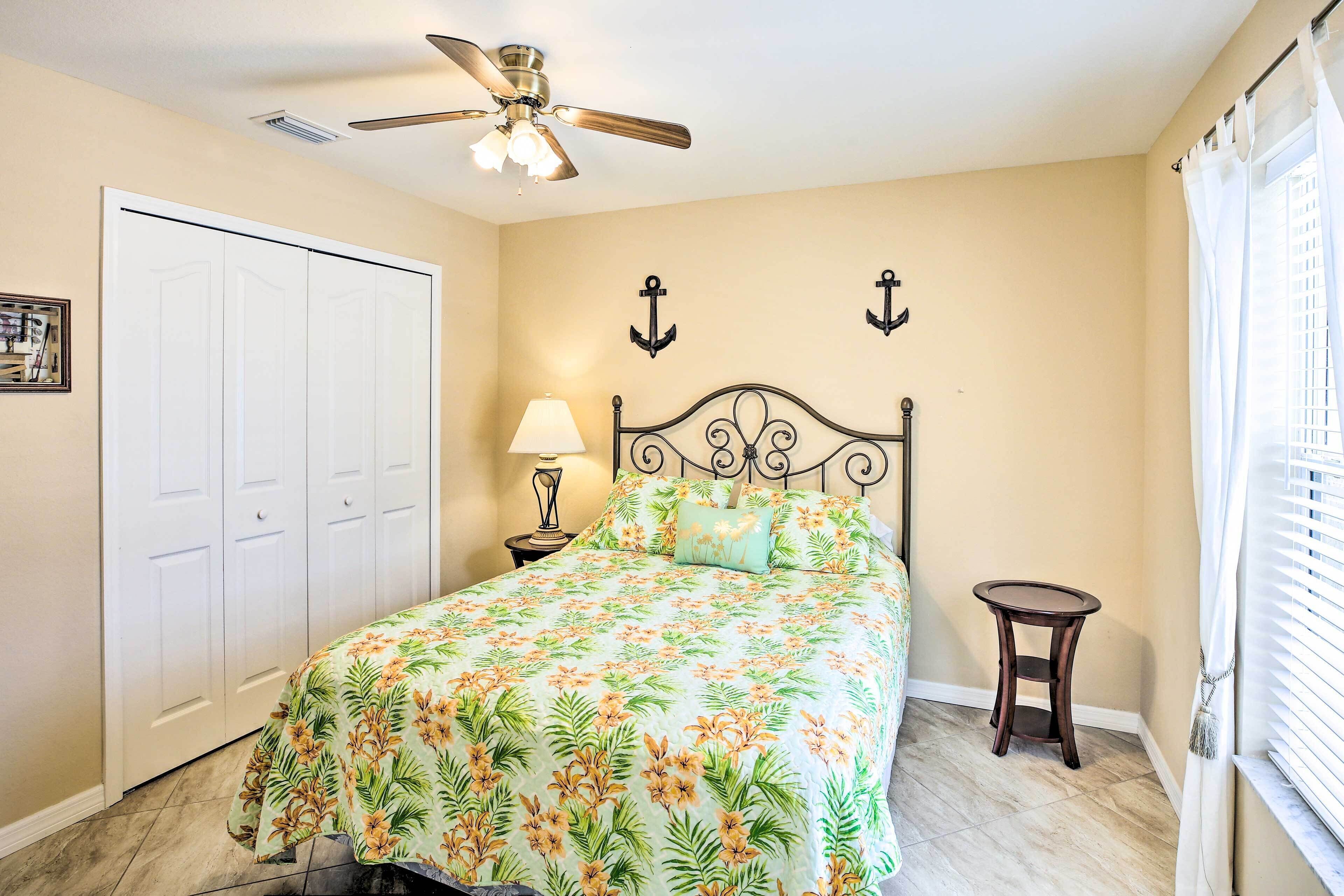 A bedroom with a bed, a ceiling fan, a nightstand, a lamp, and a window with curtains.