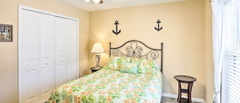 A bedroom with a bed, a ceiling fan, a nightstand, a lamp, and a window with curtains.