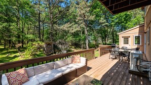 Une terrasse en bois avec un canapé et des fauteuils, donnant sur une zone boisée.
