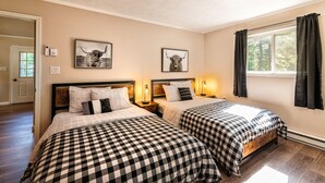 Une chambre à coucher avec deux lits, chacun agrémenté de draps à carreaux, d’une tête de lit en bois, de tables de chevet avec des lampes et de tableaux encadrés accrochés au mur.