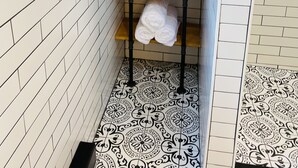 Une salle de bain avec des murs et un sol recouverts de carreaux blancs, une section de carreaux à motifs noir et blanc, un porte-serviettes avec des serviettes, un panneau et une fenêtre.