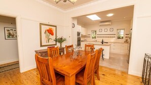 Un coin repas avec une table et des chaises en bois, un lustre et une cuisine en arrière-plan.