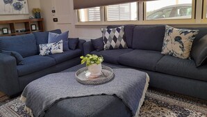 Un salon avec un canapé d’angle bleu foncé, une petite table d’appoint ornée d’une plante et un tapis à motifs.