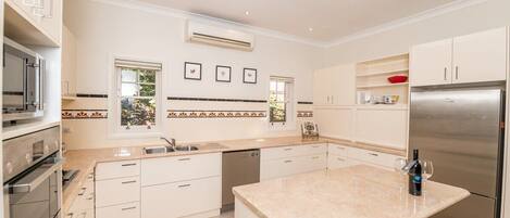 A modern kitchen with white cabinets, a stainless steel refrigerator, and a large island with a wine bottle and glasses.