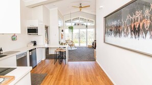 A modern kitchen with white cabinetry, a dining area with stools, a ceiling fan, and a large painting of deer. - Mortimer's Wines Loft - Adults Only Retreat (Orange)