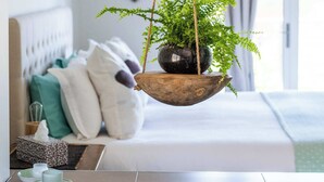 A modern hotel room with a bed, a bedside table with a plant, a heart-shaped wall decoration, and a window with curtains. - Mortimer's Wines Loft - Adults Only Retreat (Orange)