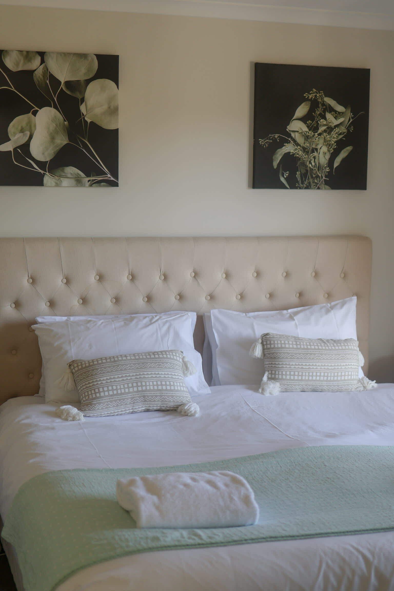 Een net opgemaakt bed met een gestuufd hoofdbord, twee kussens en een opgevouwen handdoek op een groene deken.