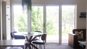 A room with a glass table, chairs, a sofa, a bookshelf, and a sliding glass door leading to an outdoor area. - Mortimer's Wines Loft - Adults Only Retreat (Orange)