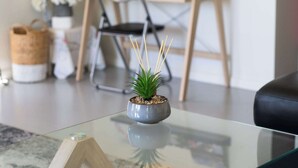 Een glazen bijzettafeltje met een kleine potplant, een boek met de titel 'Greatest Places' en een houten boekstandaard.