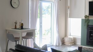 Een woonkamer met een bank, een eettafel met stoelen, een aan de muur bevestigde televisie en een schuifdeur naar een buitenruimte.